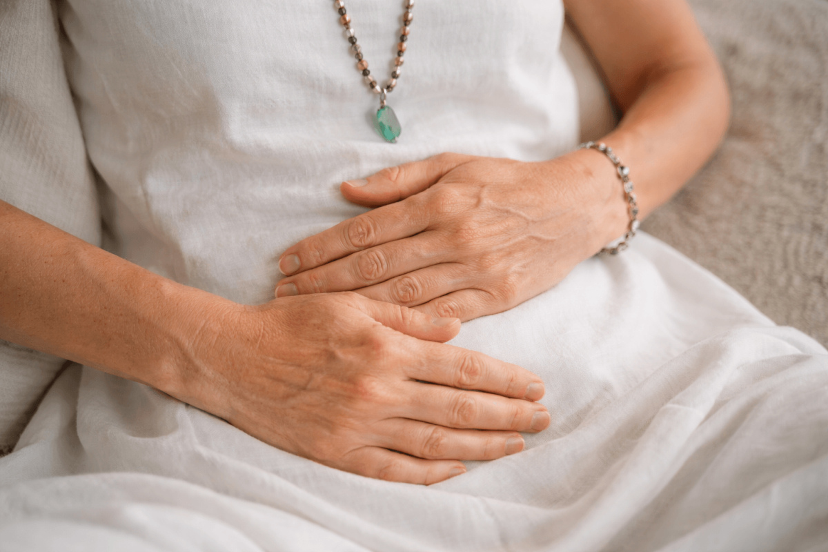 Nahaufnahme von zwei Händen, die sanft auf dem Bauch liegen, um eine beruhigende Atemübung zur Nervensystem-Regulation durchzuführen. Helle, freundliche Atmosphäre.