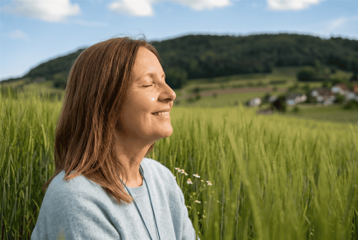 Frau in Diegten geniesst mit geschlossenen Augen die Natur und die Kraft der Zwerchfellatmung.