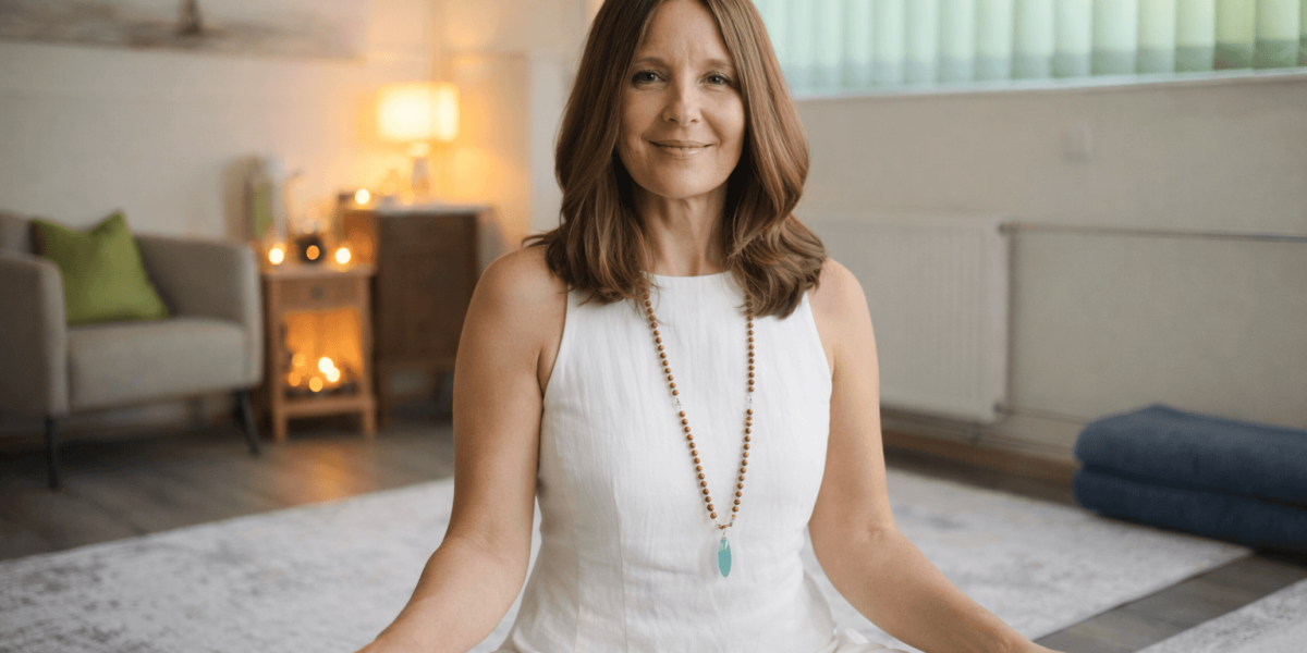 Die Atemtherapeutin Sandra sitzt im Meditationssitz in ihrer hellen, einladenden Praxis in Diegten. Sie trägt ein weisses Kleid und lächelt sanft. Im Hintergrund sieht man eine beruhigende Kerzenatmos