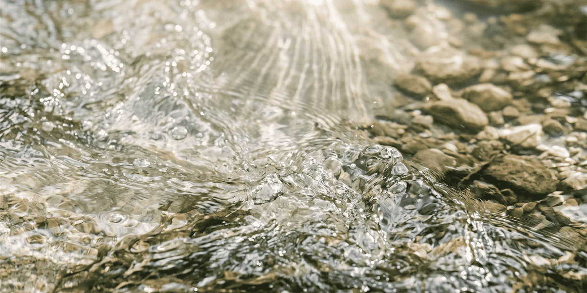 Nahaufnahme von aufgewirbeltem, klarem Wasser mit brechenden Lichtstrahlen über Kieselsteinen zur Visualisierung von Entlastung beim Breathwork.